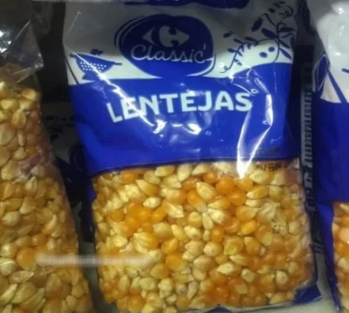 Casi 1 Bolsa de la marca Carrefour con el texto 'LENTEJAS' que erróneamente contiene granos de maíz amarillos en su interior. Se observa un claro error de envasado o etiquetado del producto.